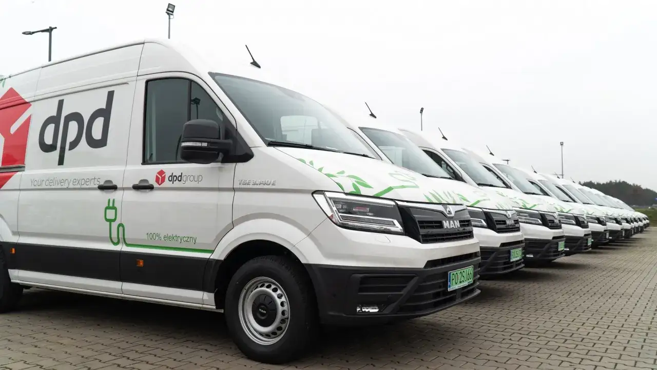 Rząd białych elektrycznych dpd bus&oacute;w, gotowych do dostarczania paczek w ekologiczny spos&oacute;b.