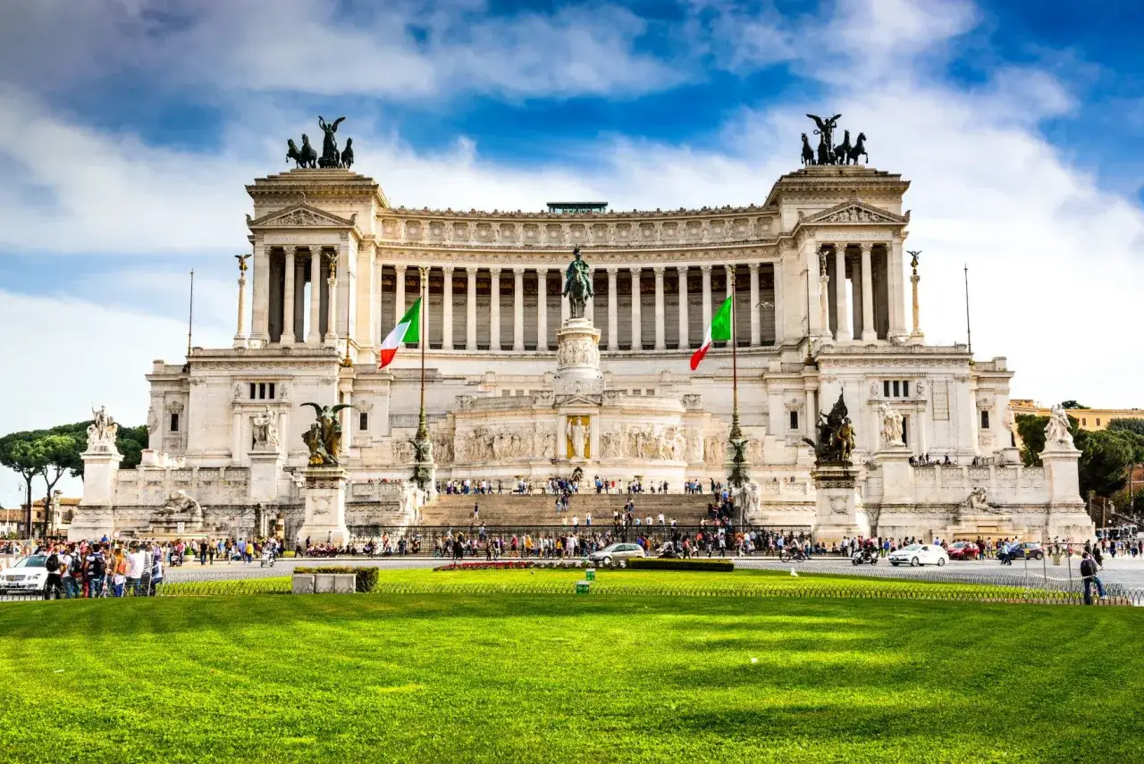 Monumentalny budynek na Piazza Venezia w Rzymie, z flagami Włoch i tłumem turystów.
