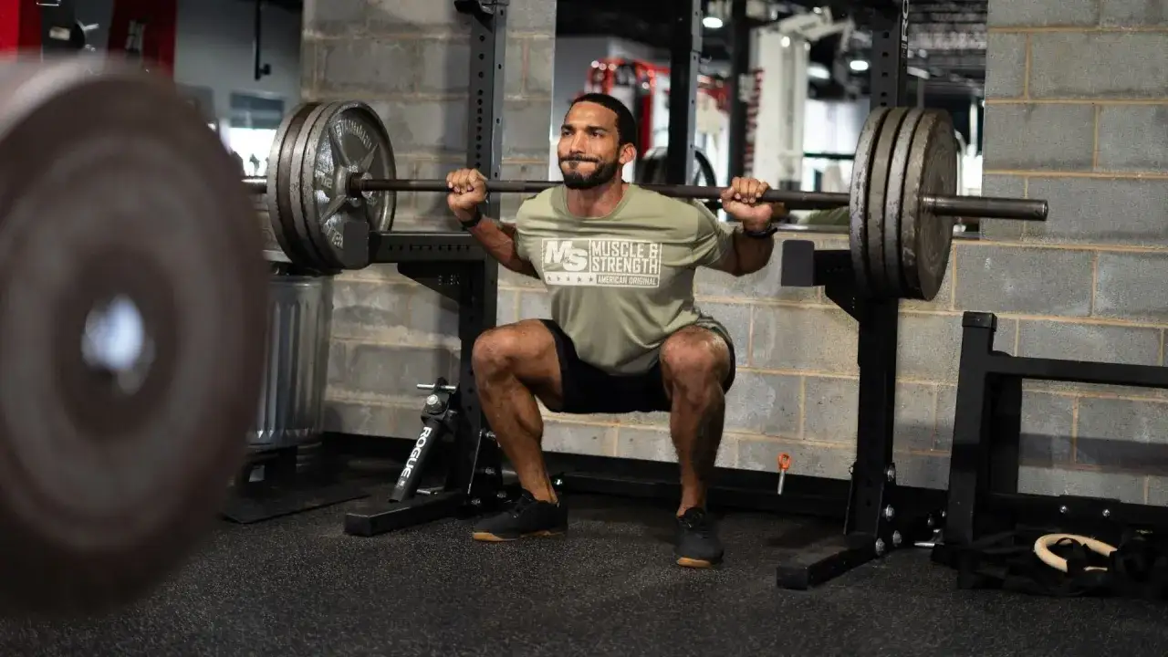 Un homme concentr&eacute; effectue un squat avec une barre charg&eacute;e dans une salle de sport. Le squat sport est un exercice de force essentiel.