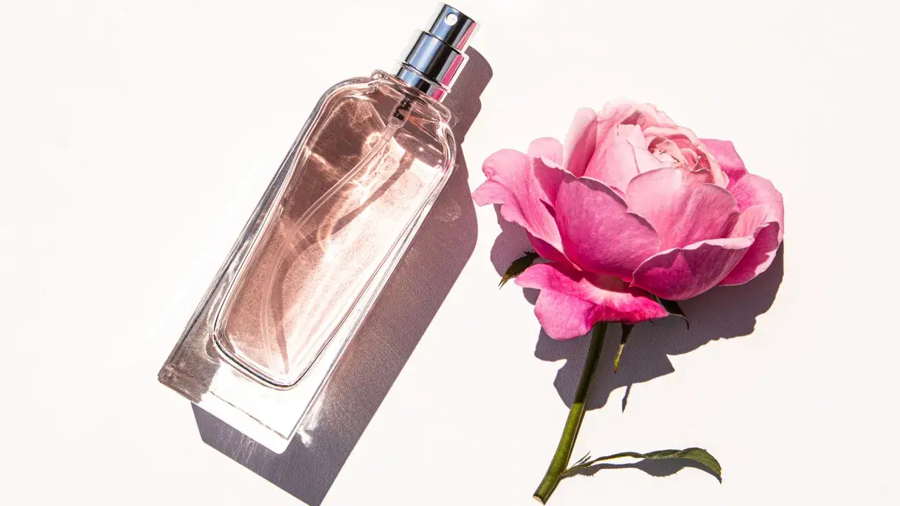 Elegancka butelka perfum De Marly Delina obok pąka różowej róży.