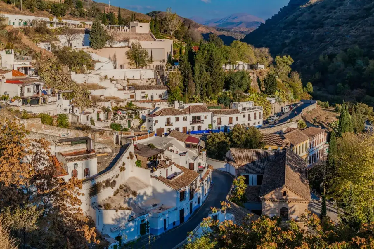 Wei&szlig;e H&auml;user schmiegen sich an H&uuml;gel im Sacromonte, Granada. Eine kurvige Stra&szlig;e schl&auml;ngelt sich durch die malerische Landschaft.