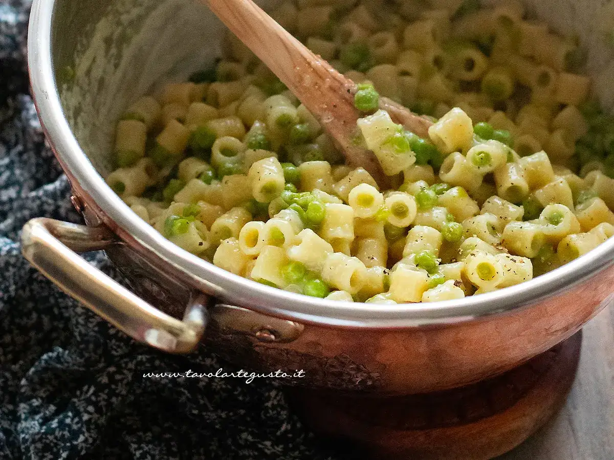 Un primo piatto cremoso di pasta e piselli, mescolato con un cucchiaio di legno in una pentola di rame.