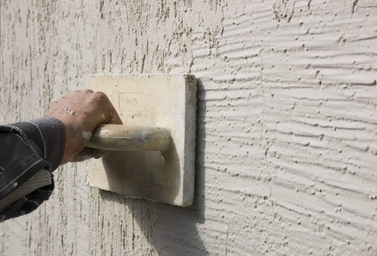 Main d'un artisan appliquant un enduit projeté texturé. Le prix au m2 varie selon la finition.