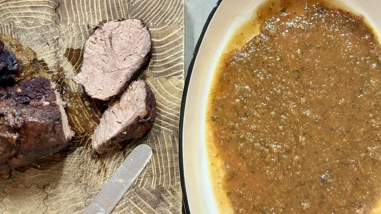 Succulento brasato di manzo affettato su un tagliere di legno, con una ciotola di sugo denso e aromatico accanto.