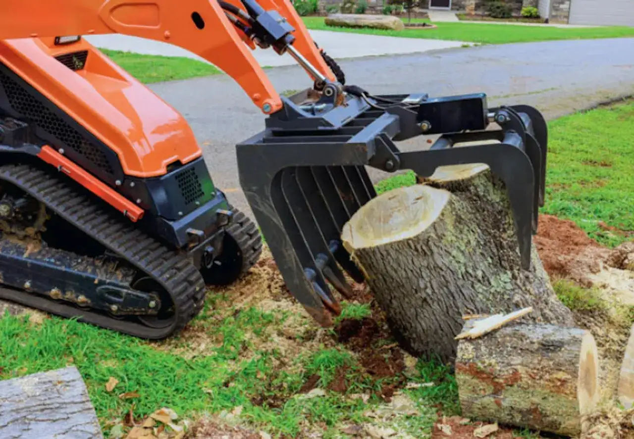 Orange minigr&auml;vare med gripklo lyfter en tr&auml;dstubbe f&ouml;r att ta bort stubbar.
