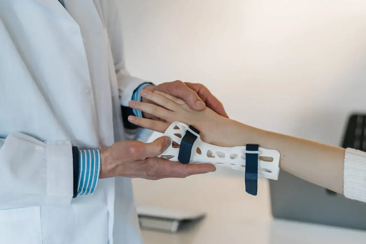 Fizjoterapeuta zakłada ortezę na nadgarstek pacjenta, co jest częścią rehabilitacji po urazie. Ćwiczenia na cieśń nadgarstka mogą pomóc w powrocie do sprawności.