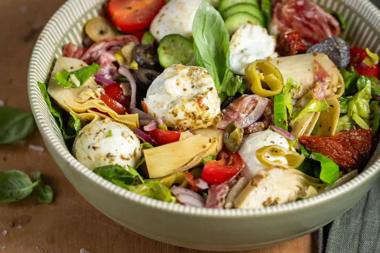 Sch&uuml;ssel mit einem frischen italienischen Salat, gef&uuml;llt mit Mozzarella-Kugeln, Artischocken, Tomaten, Oliven, Salami und Basilikum.