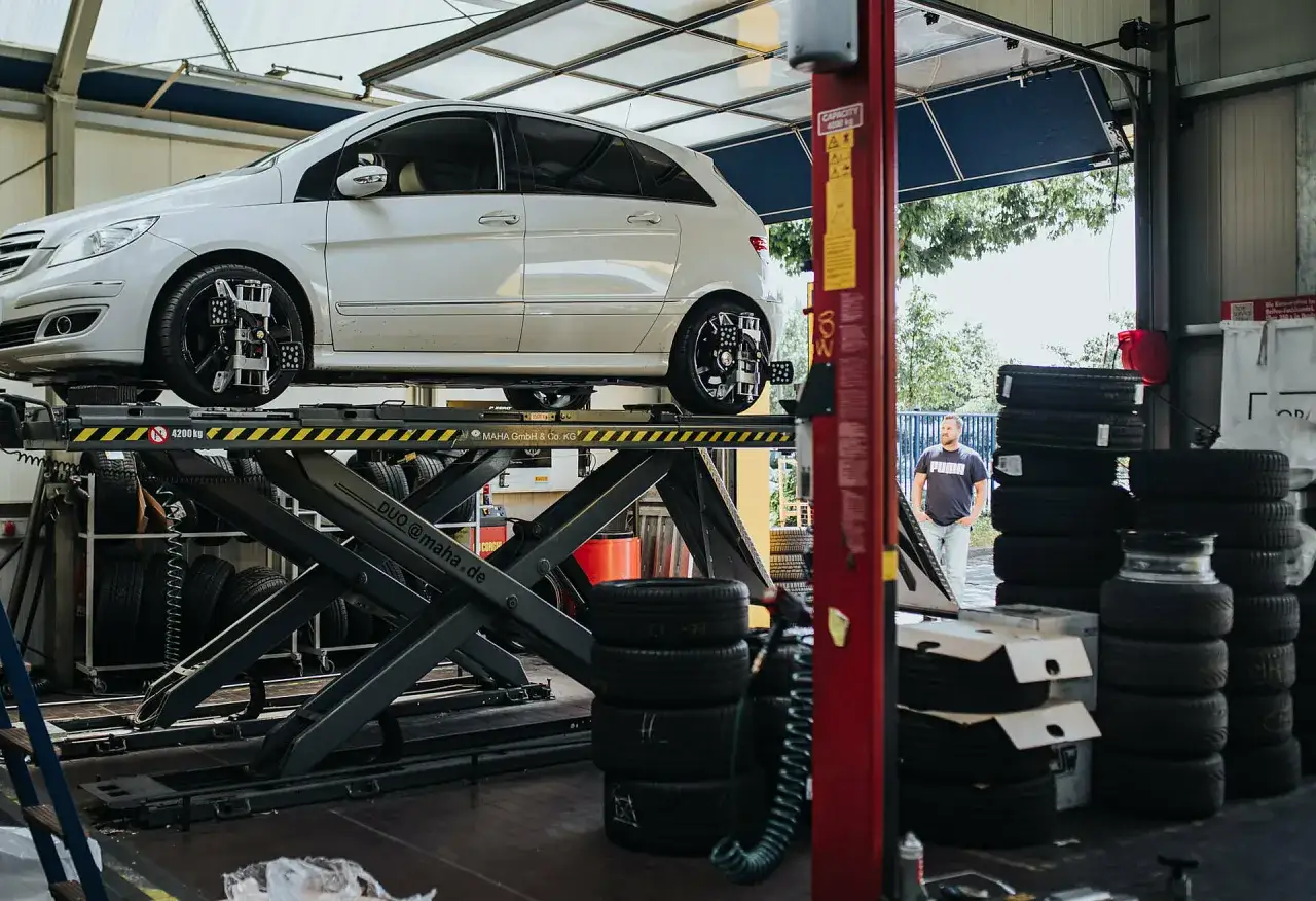 Ein Mann wartet in einer Werkstatt, während ein Auto auf einer Hebebühne steht. Die Frage