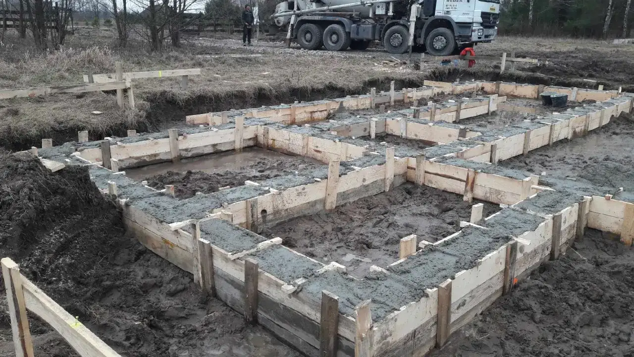 Rozpoczęła się budowa domu drewnianego. Wylano fundamenty, widać drewniane szalunki i świeży beton. W tle stoi gruszka z betonem.