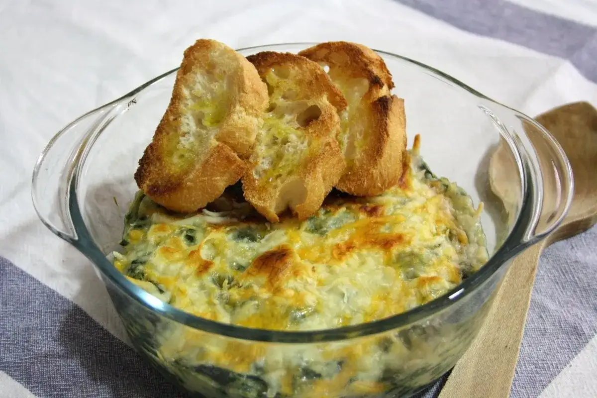 Delicioso plato de espinacas con bechamel gratinado, coronado con tostadas de pan.