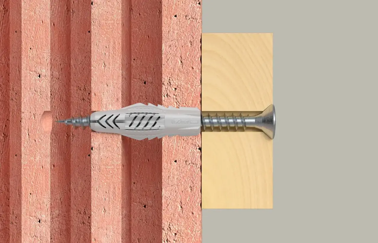 Tasselli per muri friabili: un tassello Fischer Duopower inserito in un mattone forato e fissato a un pannello di legno.
