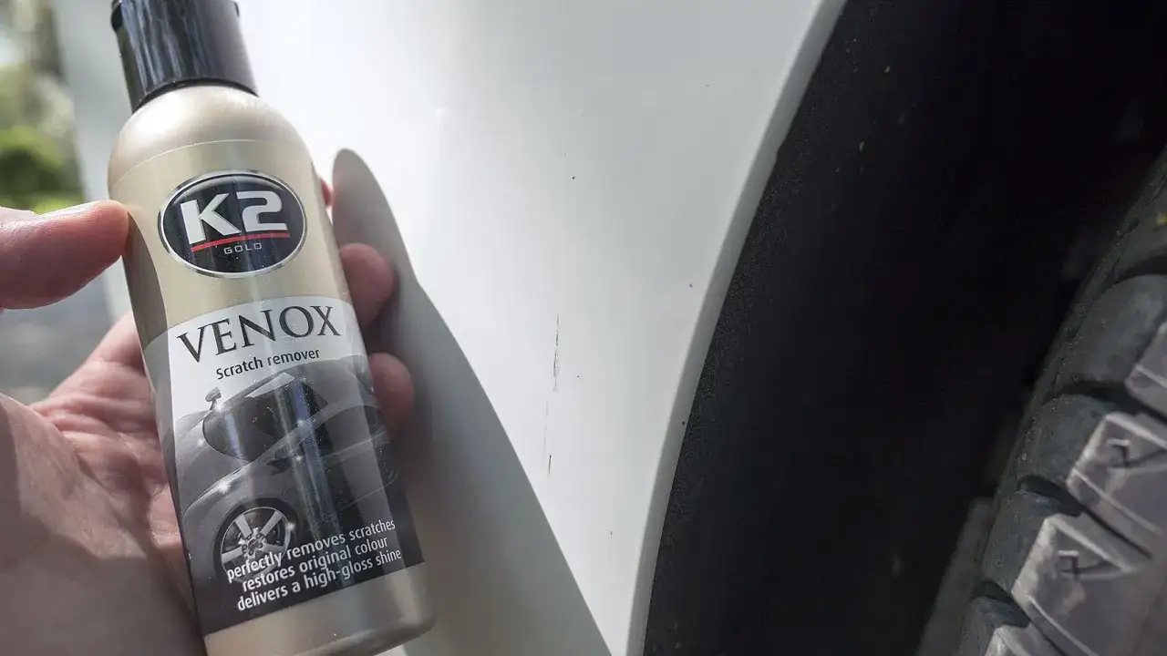 Jak usunąć rysy z samochodu domowym sposobem? Butelka K2 VENOX Scratch remover obok zarysowanego lakieru.