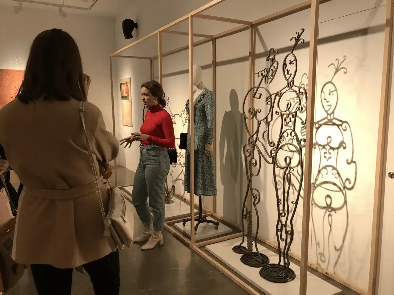Una guía explica la historia de Loewe, de donde es la marca, frente a esculturas metálicas y maniquíes en una exposición.