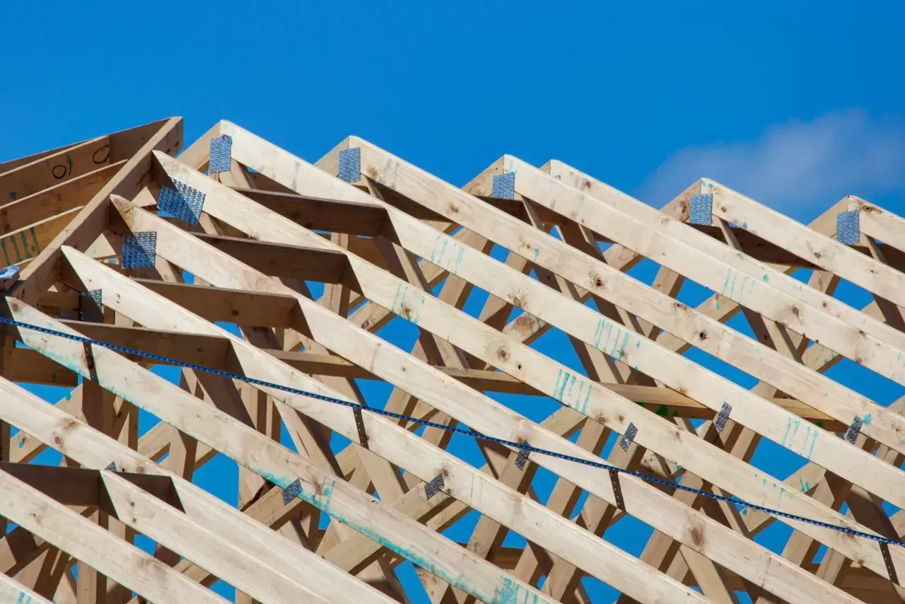Estructura de techo de madera, lista para recibir aislamiento térmico. Vigas de madera natural bajo un cielo azul brillante.