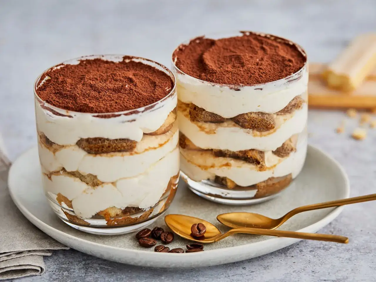 Zwei Gläser mit cremigem Tiramisu, geschichtet mit Löffelbiskuits und Kakao bestäubt. Perfekt für einen süßen Genuss.