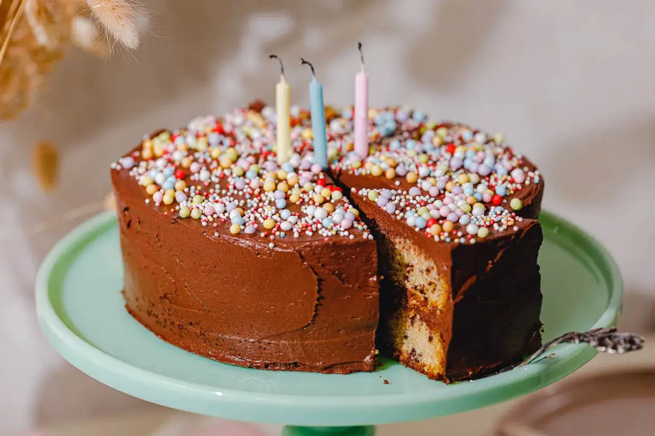 Schokoladen-Geburtstagskuchen mit bunten Streuseln und Kerzen. Ein Stück ist herausgeschnitten, das Innere zeigt Marmorkuchen. Ein tolles Geburtstagskuchen Rezept!