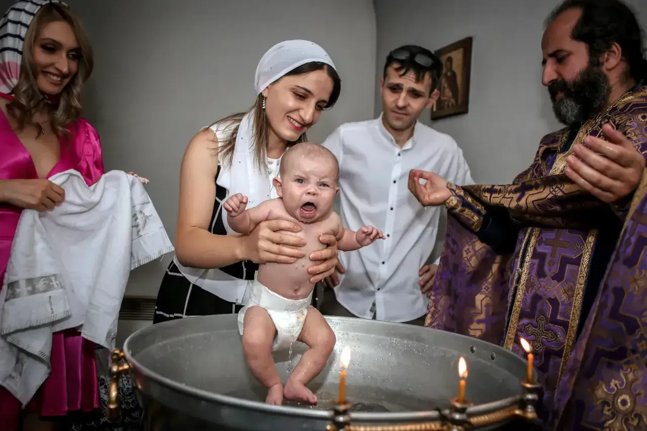Chrzest dziecka. Kapłan w szatach z krzyżami i symbolami wyjaśnia, co oznaczają symbole na paschale.