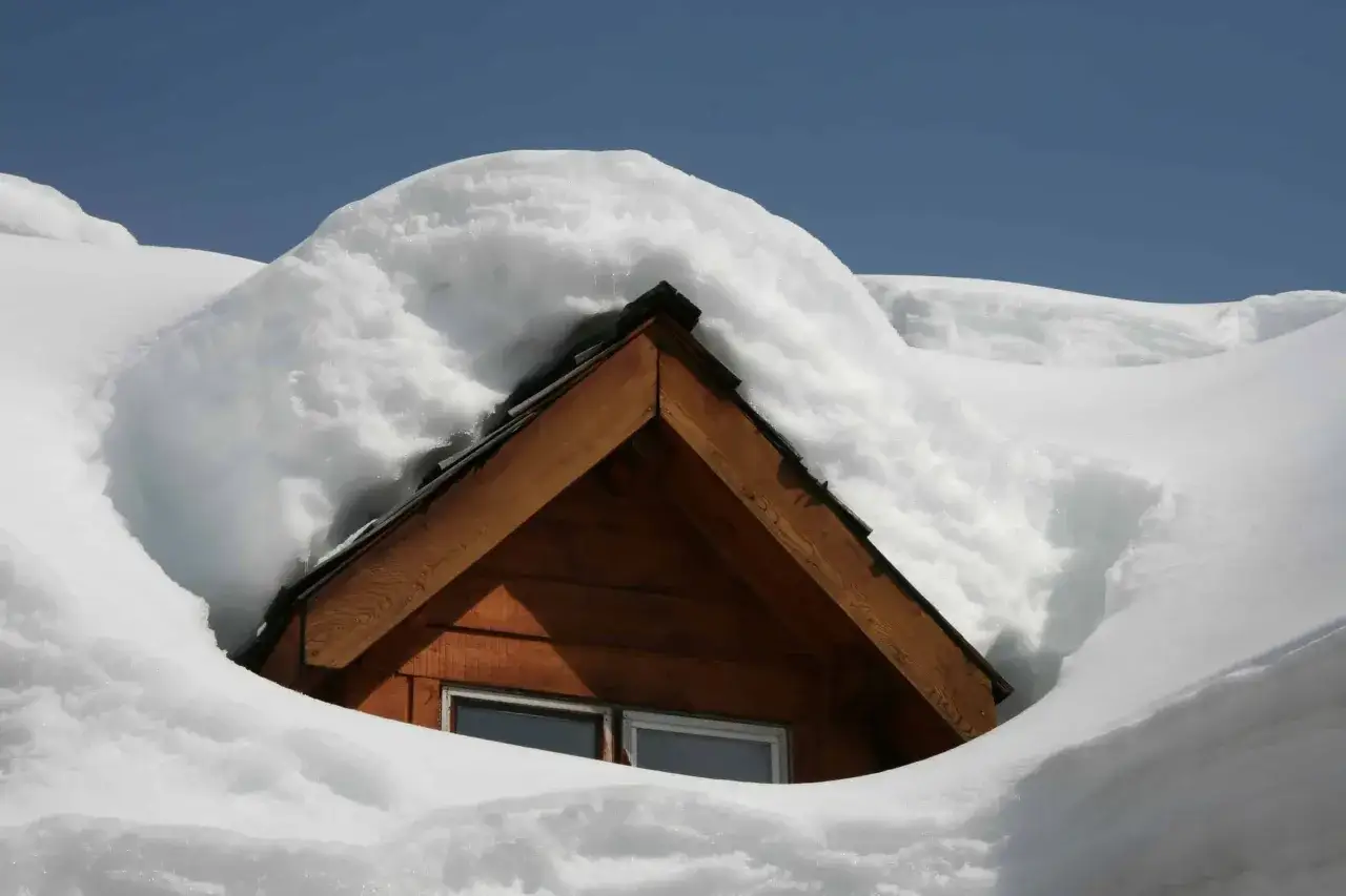 A wooden cabin roof buried under a thick blanket of snow, showcasing the challenges of cold weather roofing.