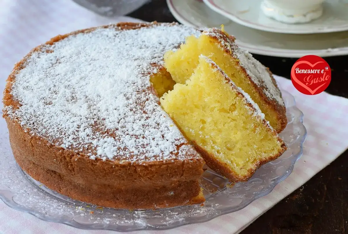 Una soffice torta allo yogurt, cosparsa di zucchero a velo, con due fette tagliate per mostrare la sua morbidezza.