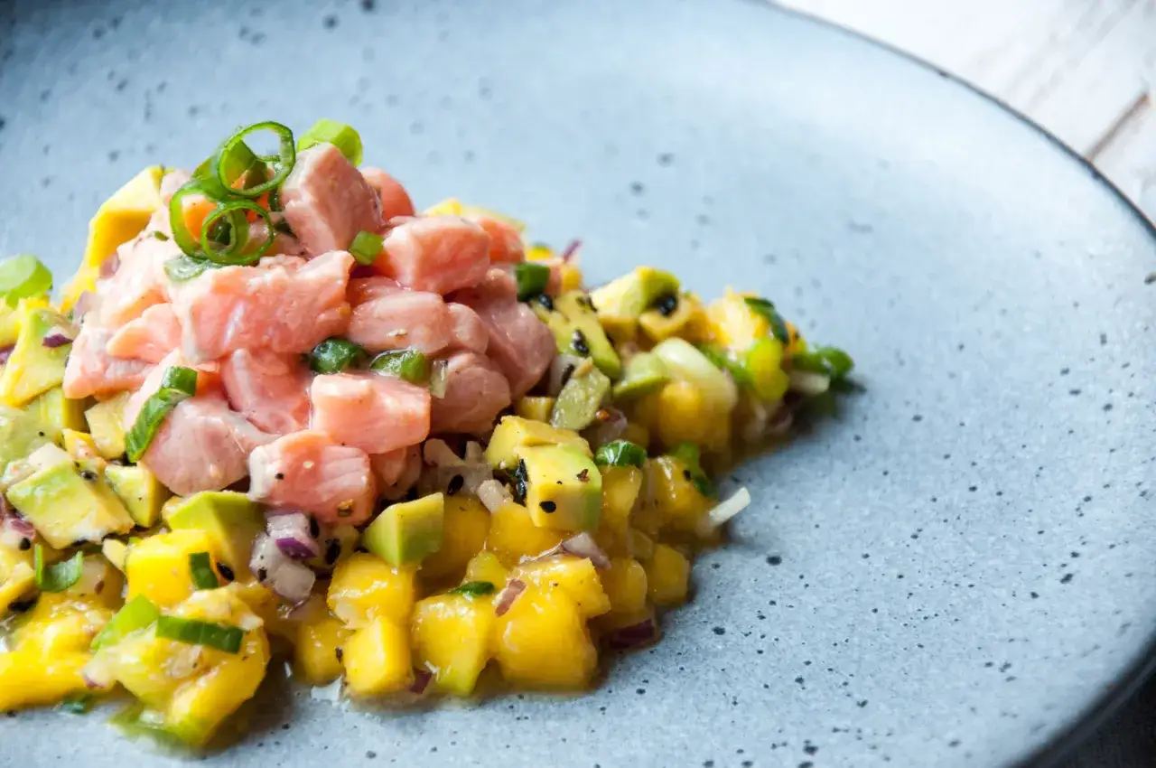 Kolorowe ceviche z łososia z awokado i mango, ozdobione szczypiorkiem, na szarym talerzu.