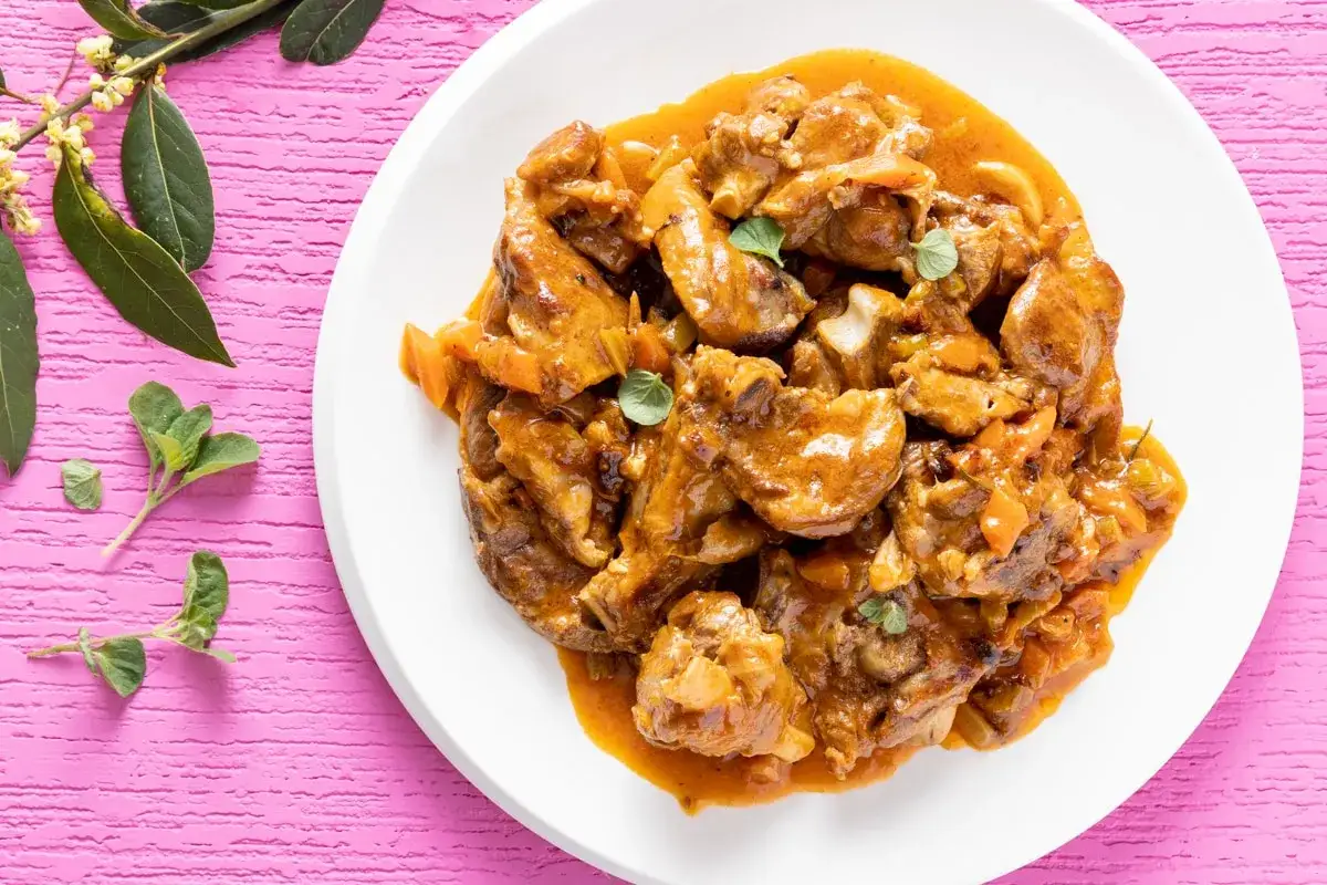 Agnello in umido succulento, un'idea perfetta per imparare come cucinare l'agnello in umido. Servito su un piatto bianco con erbe aromatiche.