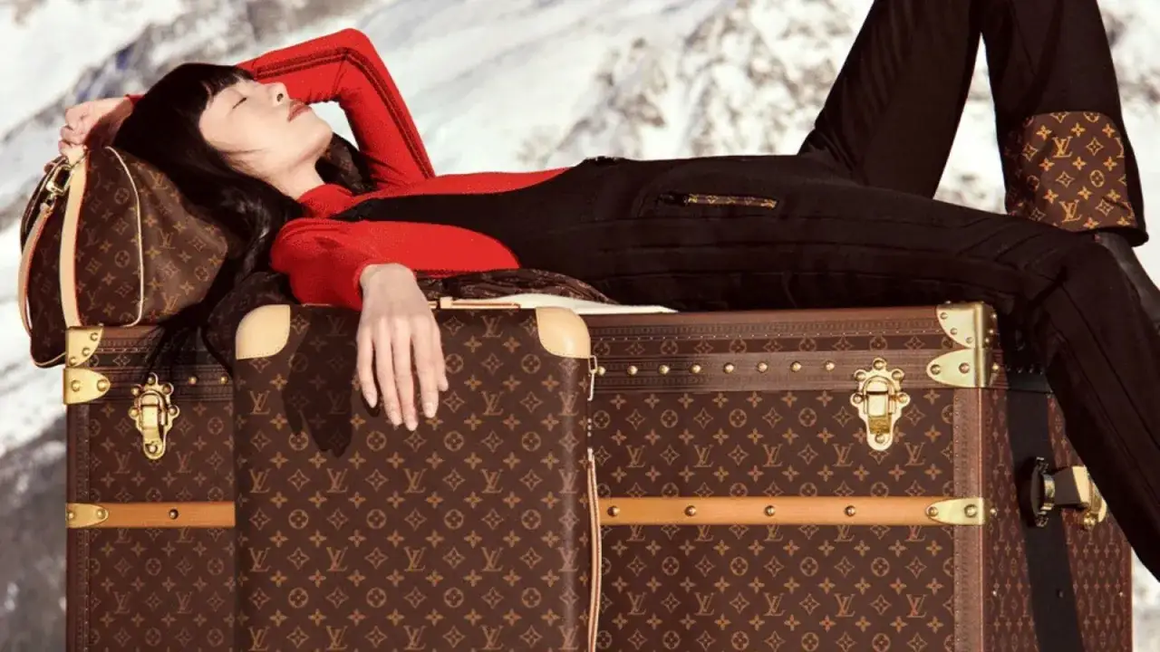 Donna sdraiata su bauli con il logo del marchio Louis Vuitton, in un paesaggio innevato.