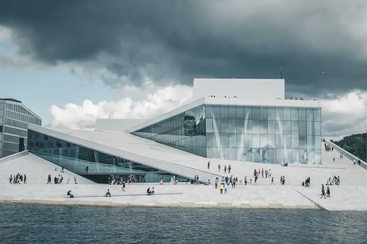 Nowoczesna opera w Oslo z pochyłymi dachami i szklanymi fasadami, po których spacerują ludzie.