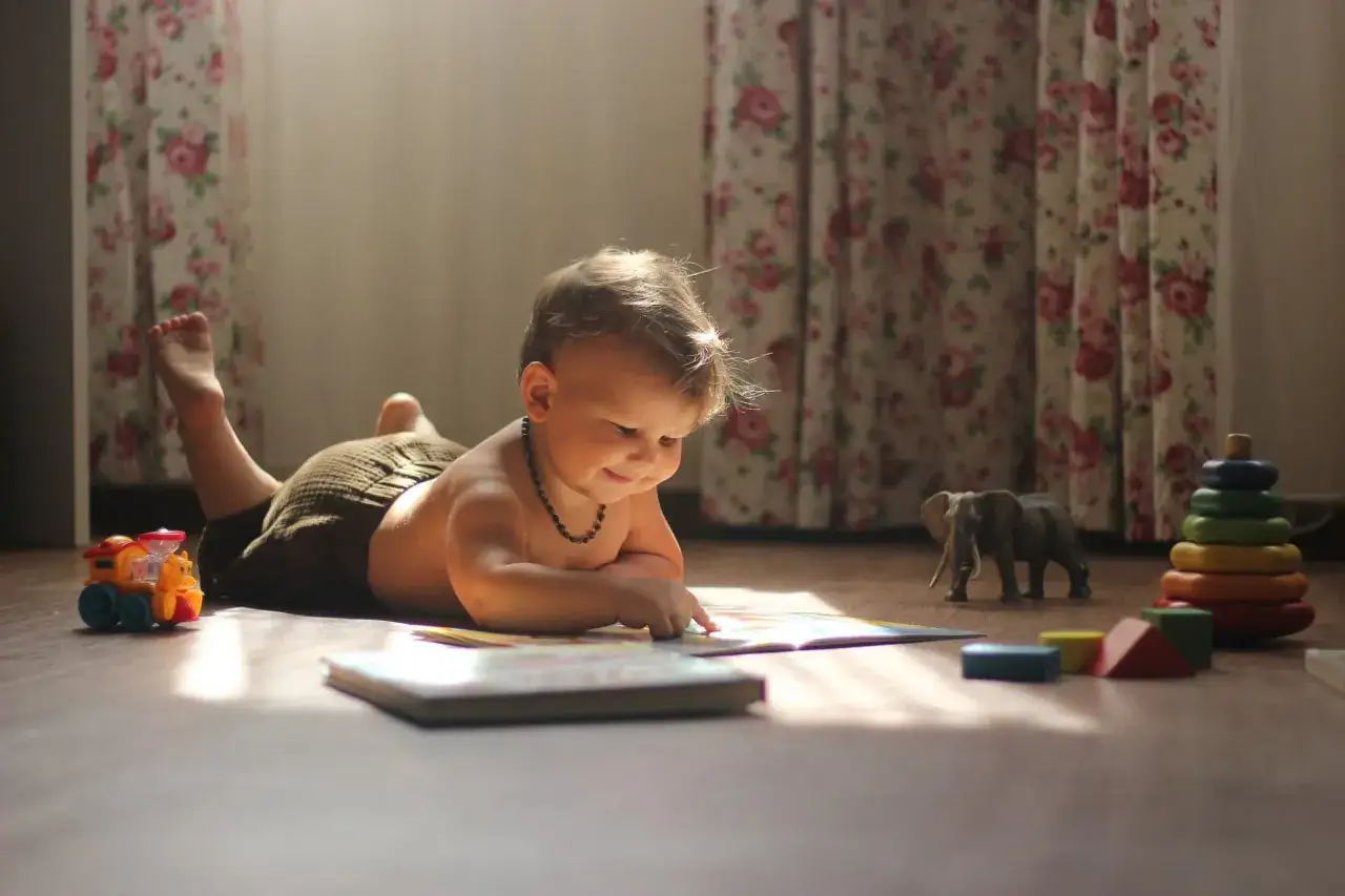 niemowlę na macie edukacyjnej unosi gł&oacute;wkę i sięga po zabawkę