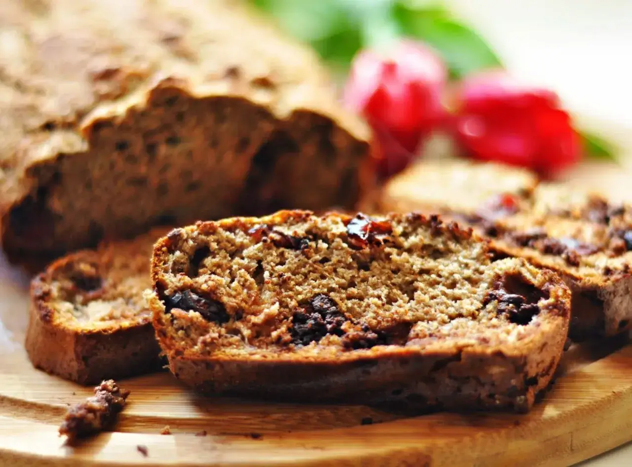 Pokrojony chlebek bananowy bez cukru z kawałkami czekolady i rodzynkami, na drewnianej desce.