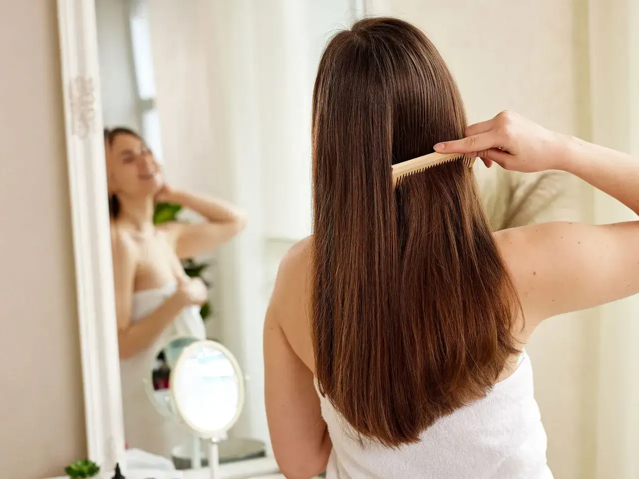 Mujer se peina el cabello largo y castaño con un peine de madera, soñando con cómo hacer que el pelo crezca rápido.