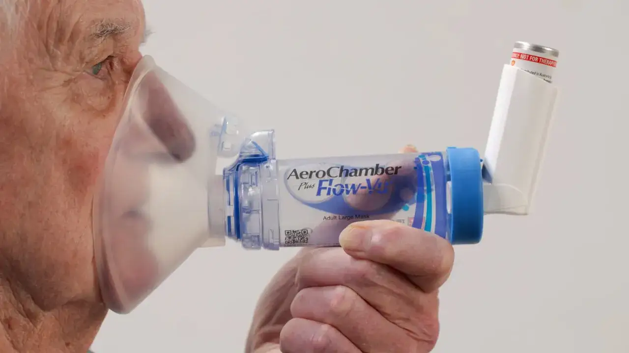&Auml;lterer Mann nutzt ein AeroChamber-Inhalator mit Maske zur Linderung von Allergien. Der Spray gelangt so direkt in die Lunge.