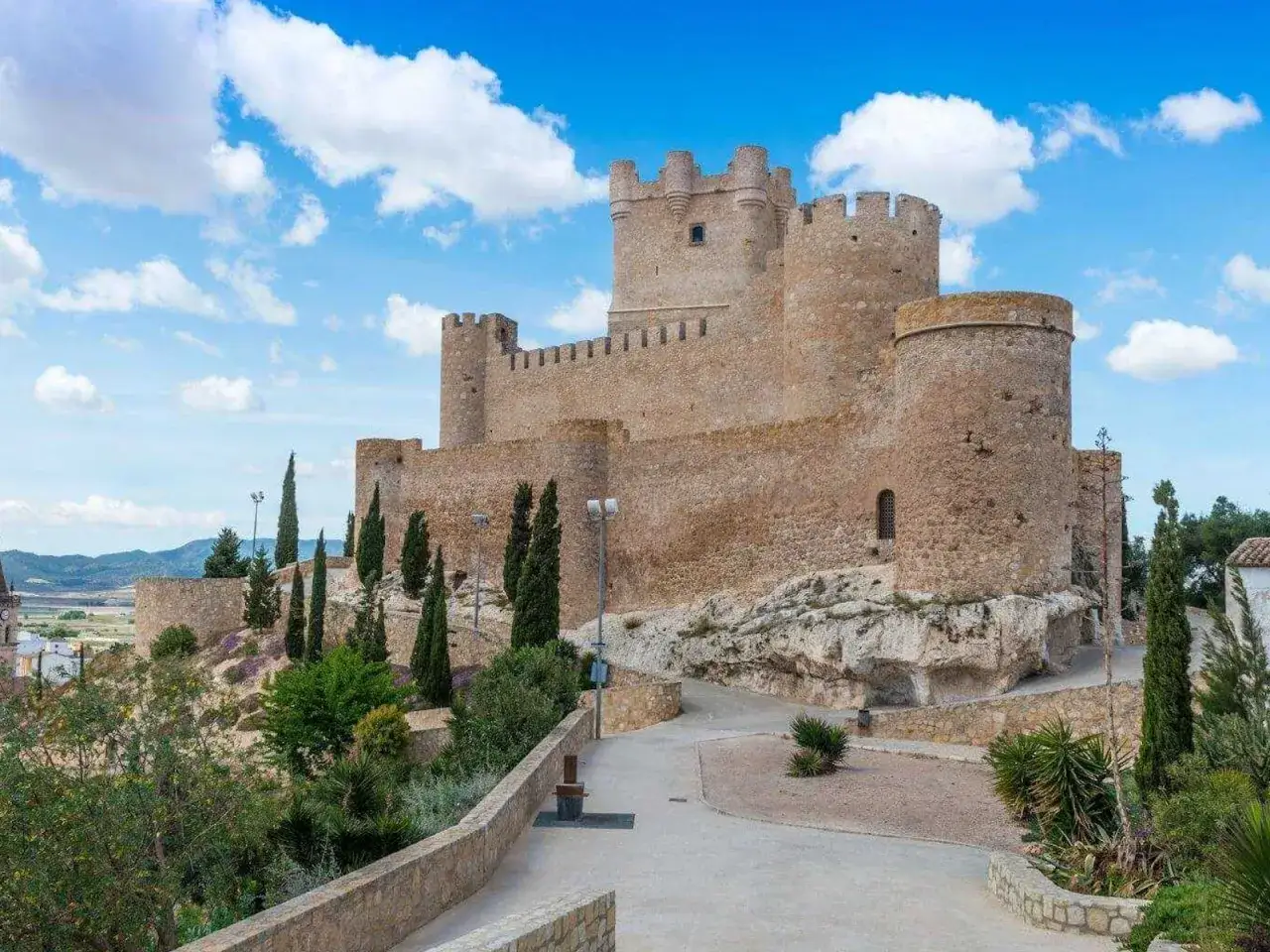 Castillo de Almansa, parte de la ruta de la lana, se alza majestuoso sobre una colina rocosa bajo un cielo azul con nubes blancas.