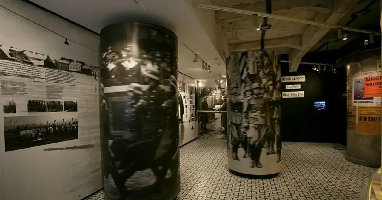Wystawa w fabryce emalia Oskara Schindlera. Cylindry z historycznymi zdjęciami i nazistowskie symbole na podłodze.
