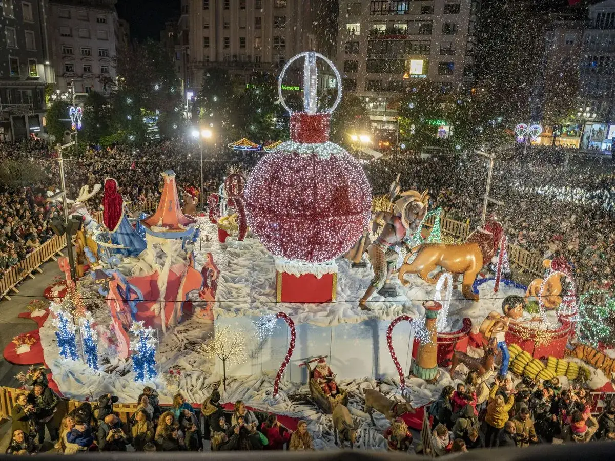 Espectacular desfile navideño con el encendido de luces en Santander. Una gran bola de Navidad adorna la carroza, rodeada de figuras y una multitud entusiasta.