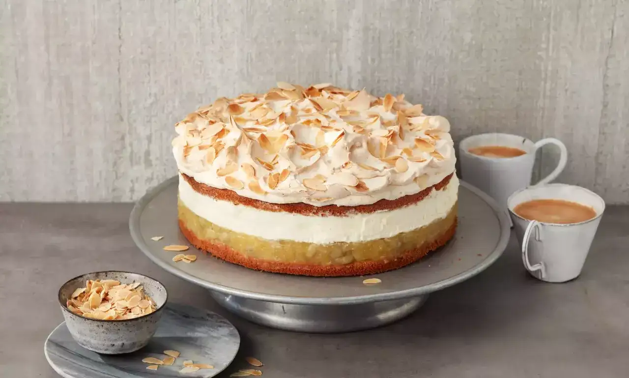 Eine k&ouml;stliche Hansen Jensen Torte mit Baiserhaube und Mandelsplittern, serviert mit zwei Tassen Kaffee.