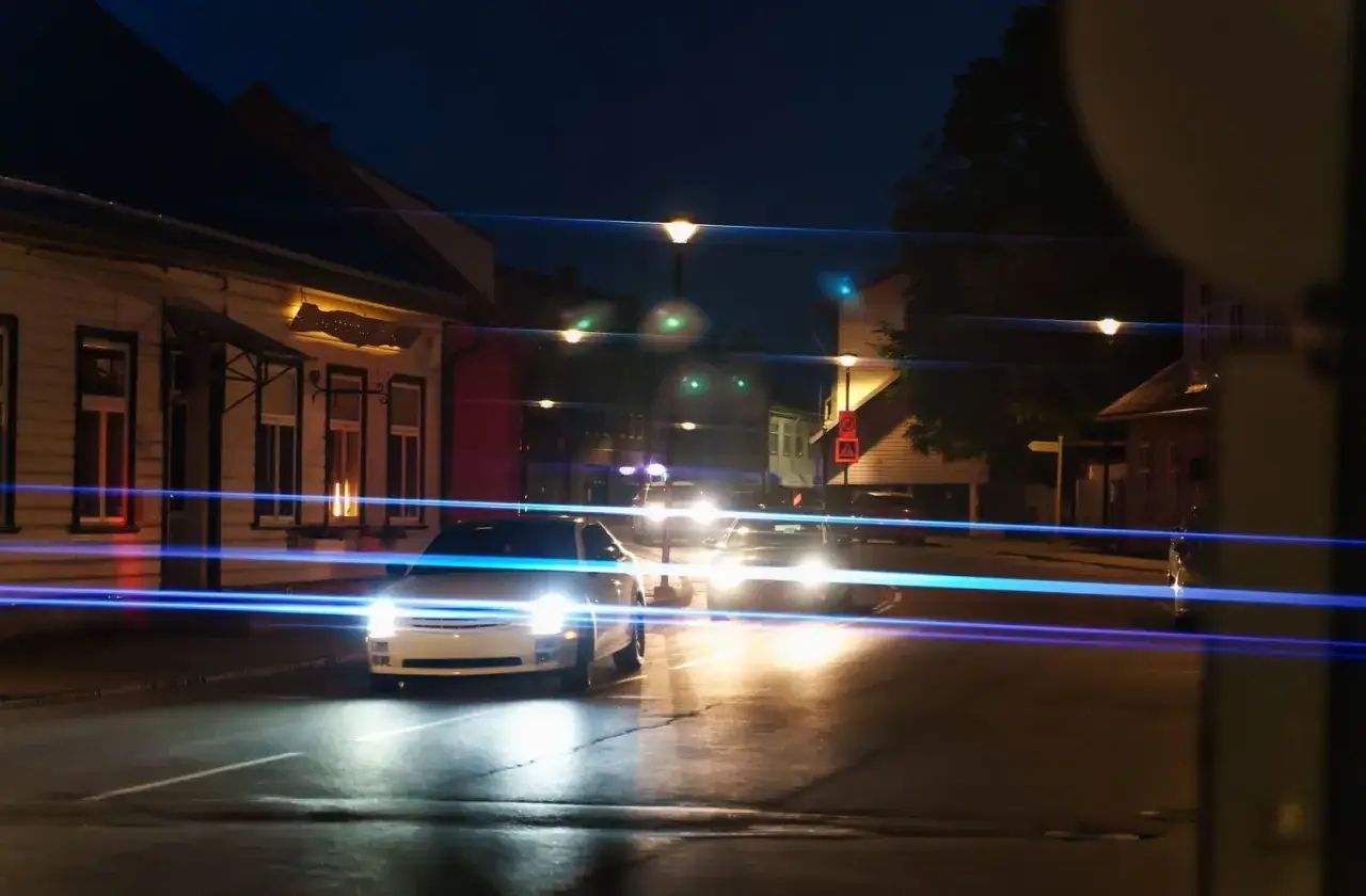 Strada notturna con auto e lampioni. Le luci dei fari creano un effetto di astigmatismo, allungandosi in strisce luminose.