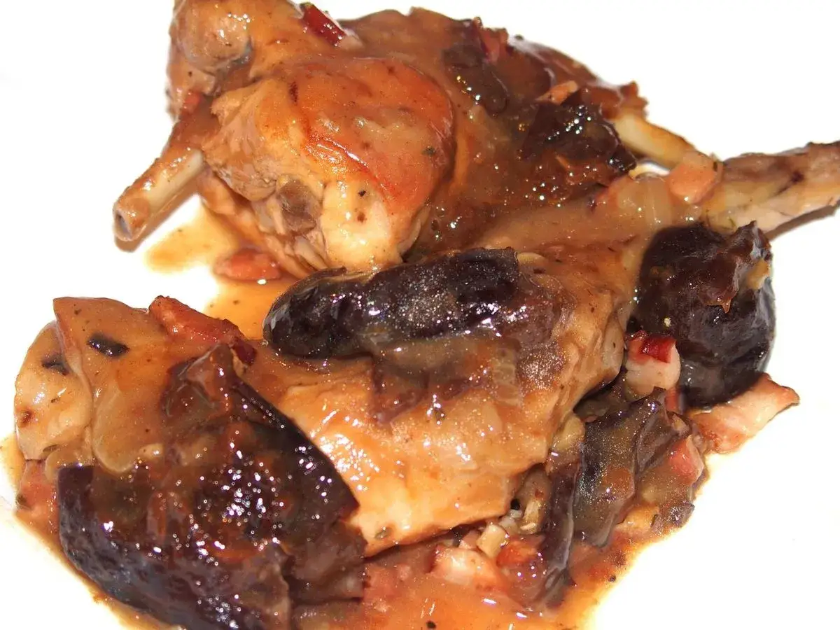 Un plat savoureux de lapin aux pruneaux, mijoté dans une sauce riche et brune, avec des morceaux de viande tendres et des fruits foncés.