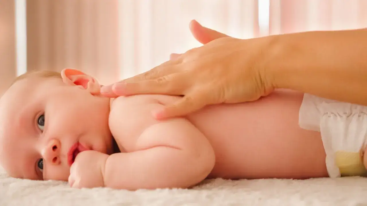 Una mano acaricia la espalda de un bebé, ofreciendo un reconfortante masaje infantil.