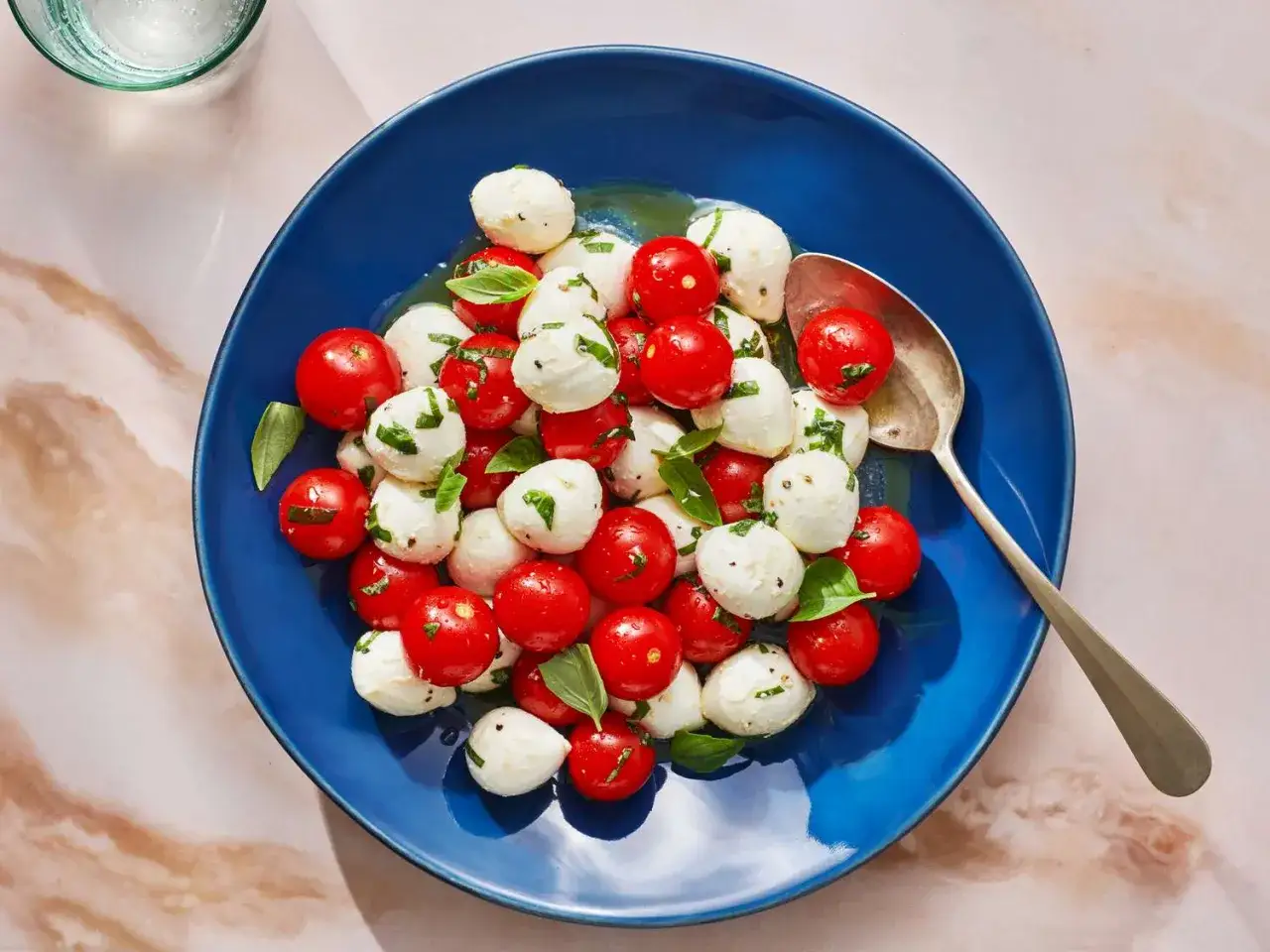 Tomate Mozzarella Salat mit frischem Basilikum auf blauem Teller, appetitlich angerichtet.