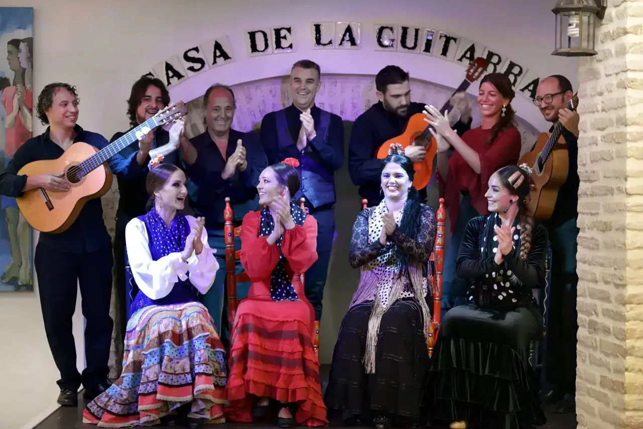Grupo de artistas flamencos, con guitarras y bailaoras, celebrando en el escenario de la Casa de la Guitarra.