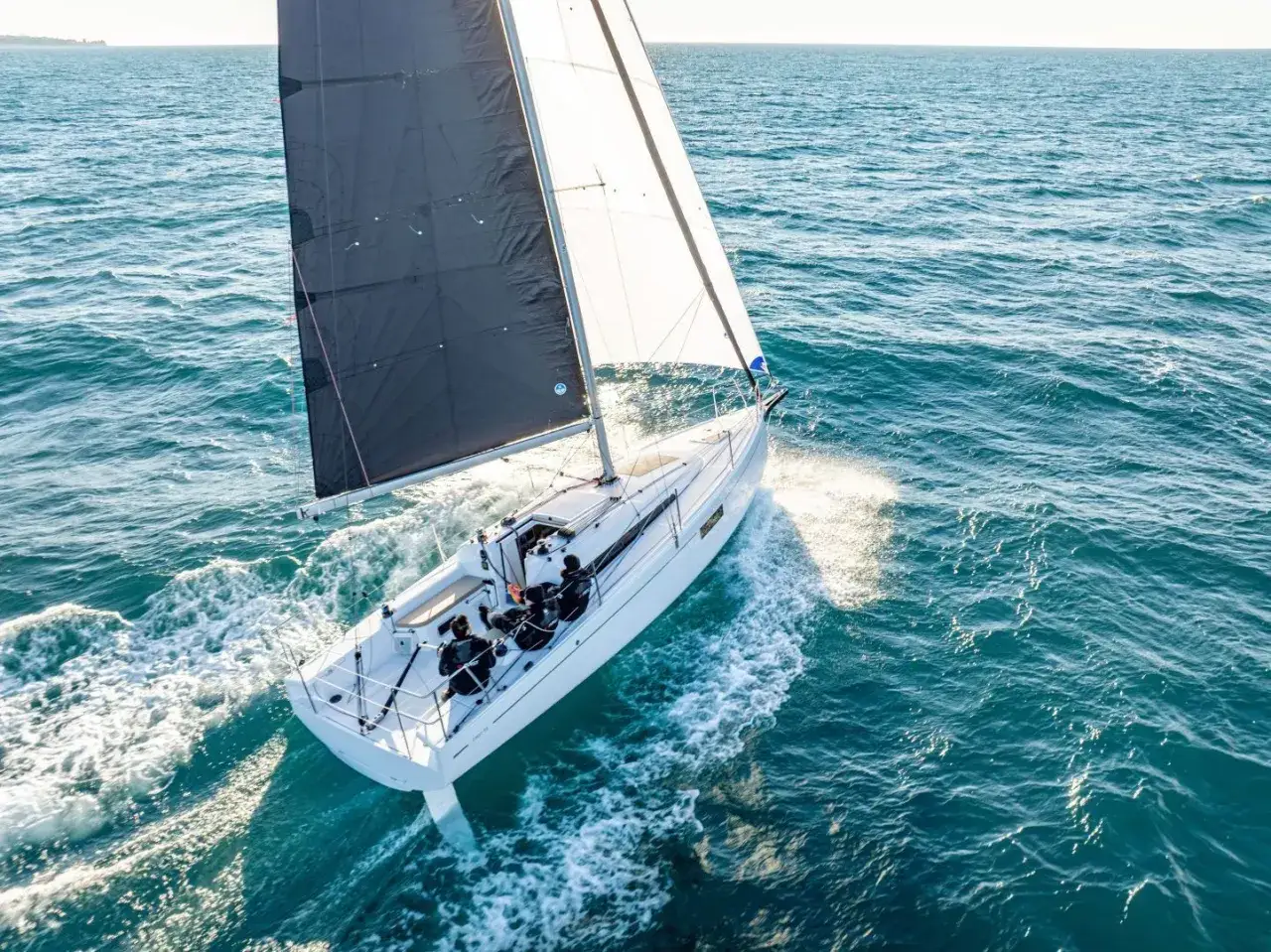 Voilier blanc naviguant sur une mer bleue, avec une voile noire et une voile blanche gonflées par le vent. Les premières 30 fiches techniques de ce modèle sont disponibles.