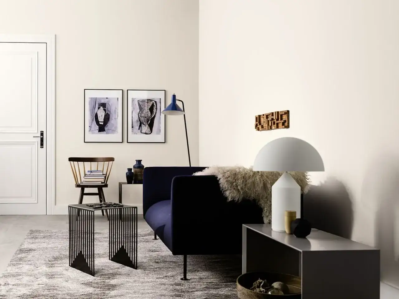 Ein Wohnzimmer mit dunklem Sofa, Holzsessel und Kunstwerken an **hellen Wandfarben**. Ein moderner Tisch und eine Lampe runden das Bild ab.