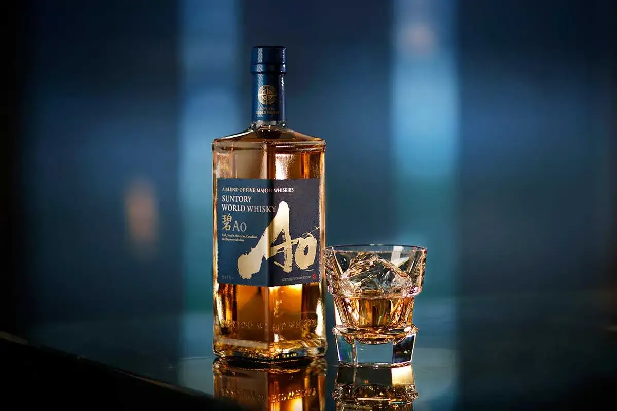 Suntory World Whisky AO, ein Blend aus fünf Whiskys, steht neben einem Glas mit Eis und dem bernsteinfarbenen Whisky.