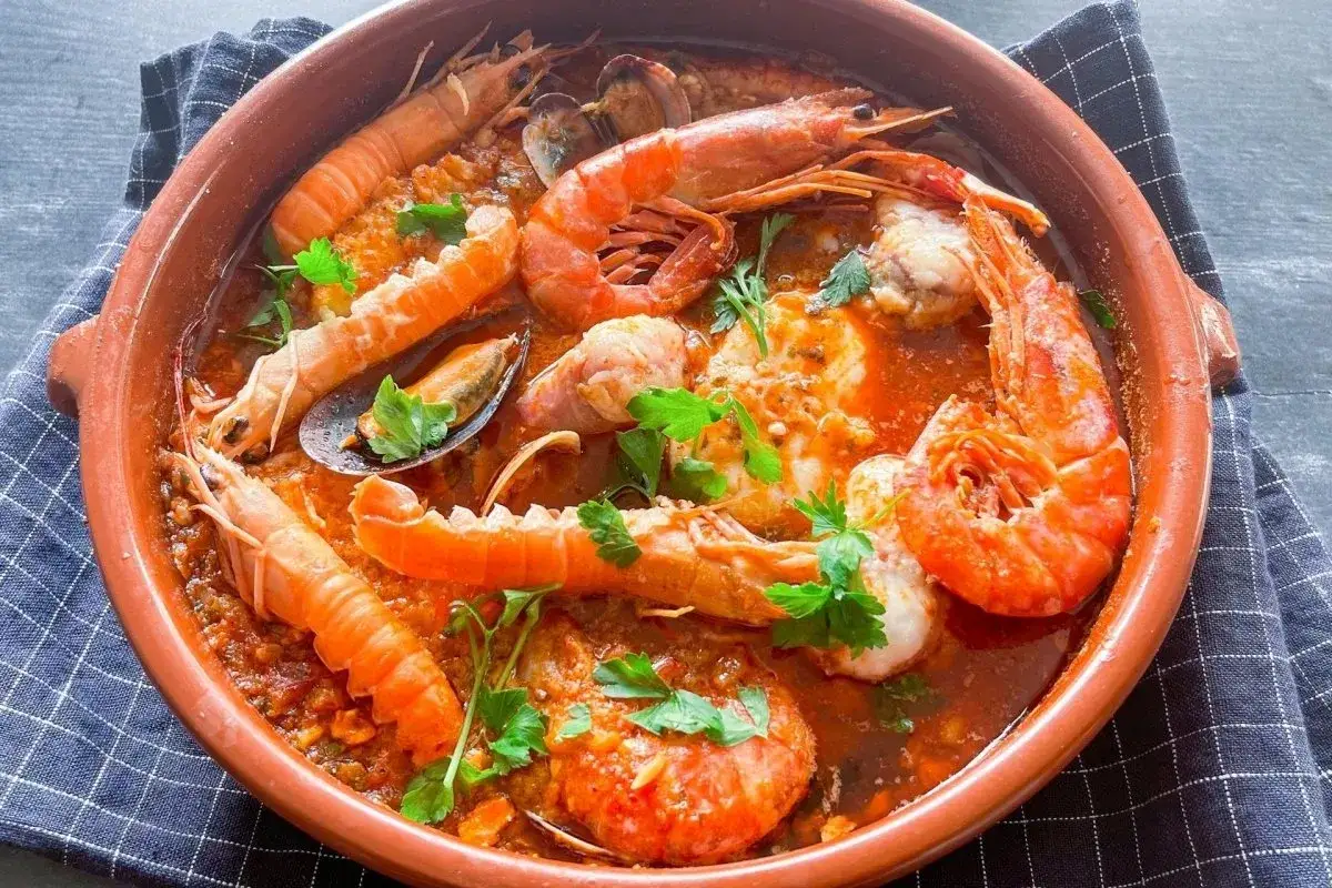 Deliciosa zarzuela de pescado con gambas, cigalas y mejillones en una cazuela de barro, decorada con perejil fresco.