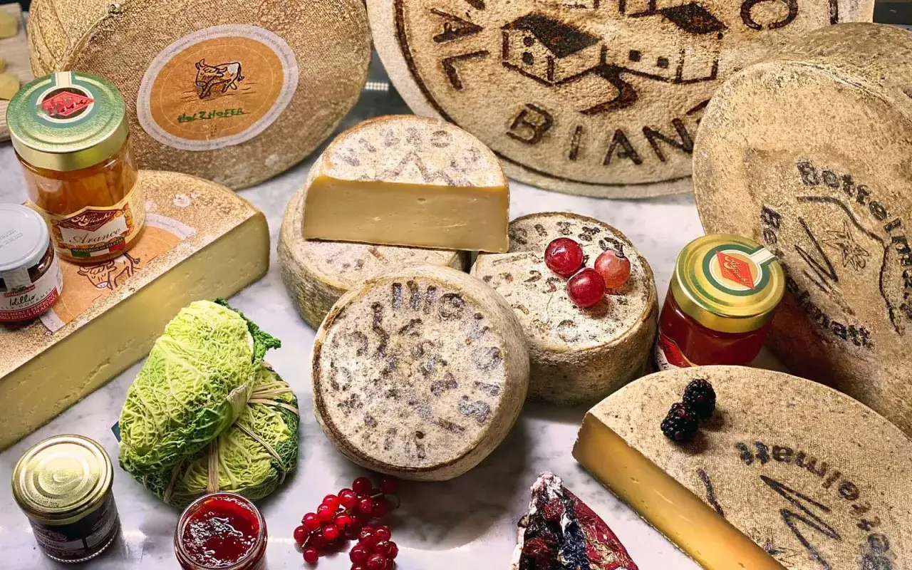 Variet&agrave; di formaggi di montagna, alcuni interi, altri affettati, con confetture, uva e ribes.