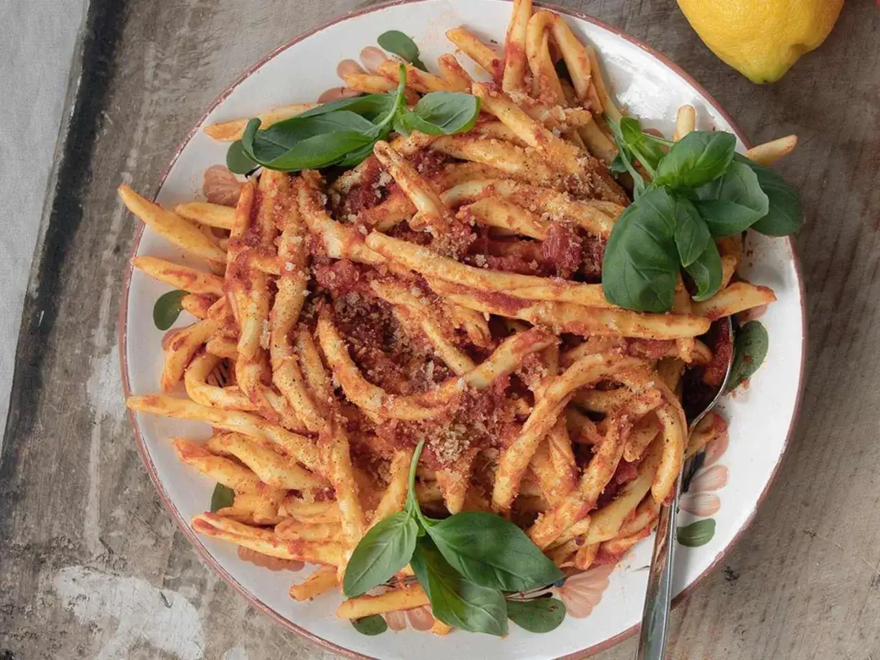 En tallrik med nduja pasta, toppad med färsk basilika och en citronskiva i bakgrunden.