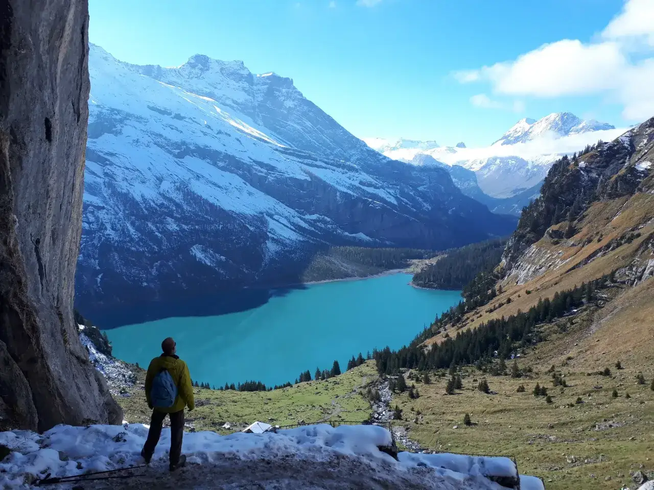 Ein Wanderer blickt auf einen türkisfarbenen See vor schneebedeckten Bergen. Ein perfektes reiseziel schweiz für Naturliebhaber.