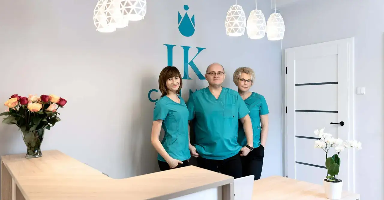 Trzy osoby w turkusowych uniformach stoją za ladą recepcji w klinice.