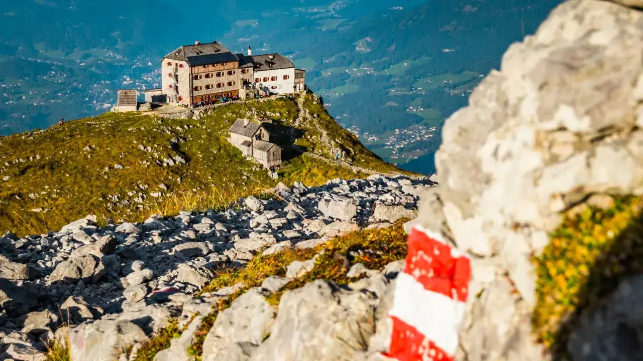 Bergsteigerhütte auf einem Gipfel, ideal für eine Watzmannhaus Wanderung. Rot-weiße Markierung auf Felsen weist den Weg.