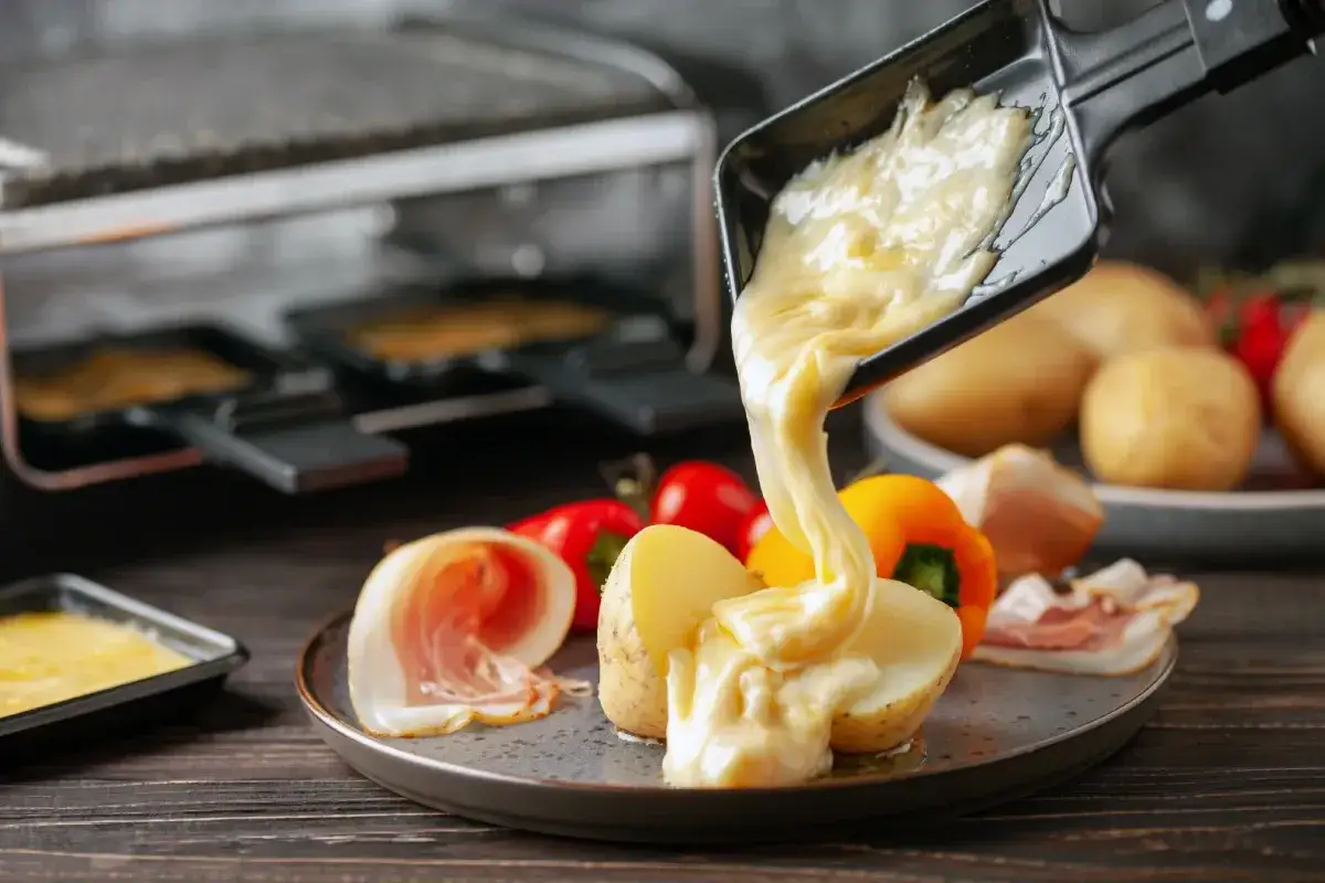 Formaggio fuso in padella, filante e dorato, viene versato su patate e salumi. Un piatto invitante e gustoso.